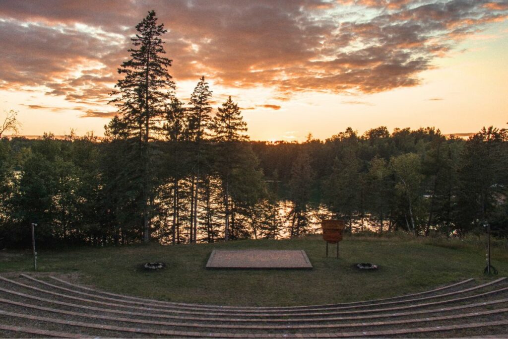 A pink sunset and pine trees in shadow with outdoor amphitheater in foreground