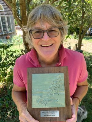 A woman wearing glasses holds an award plaque and smiles into the camera