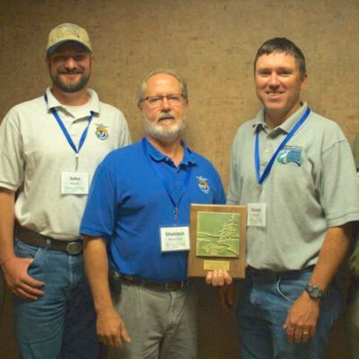 Three men wearing polo shirts pose for a photo holding an award plaque
