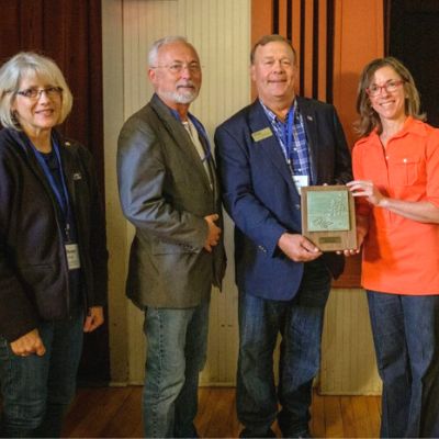 Four people pose for a photo, smiling, with an award plaque